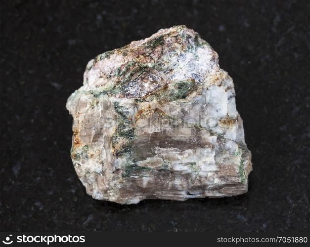 macro shooting of natural mineral rock specimen - rough Delhayelite stone on dark granite background from Yuksporr, Khibiny Mountains, Kola Peninsula, Russia