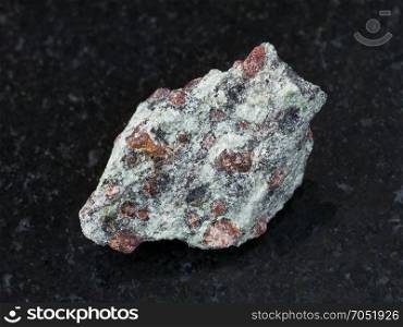 macro shooting of natural mineral rock specimen - rough eclogite stone on dark granite background from Salma region, Kola peninsula, Russia