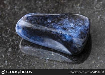 macro shooting of natural mineral rock specimen - tumbled dumortierite gem on dark granite background