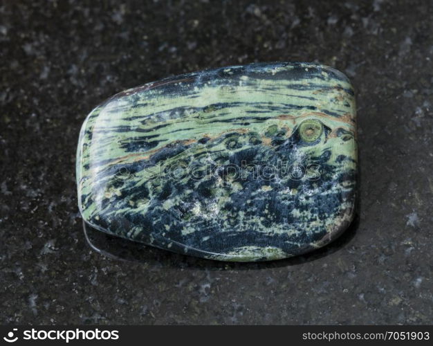 macro shooting of natural mineral rock specimen - tumbled rhyolite gemstone on dark granite background from Madagascar