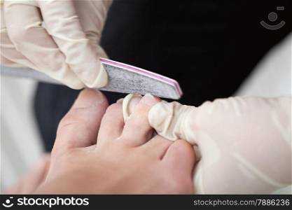 Macro shot of a beautician in gloves filing female nails. Professional pedicure at beauty treatment salon