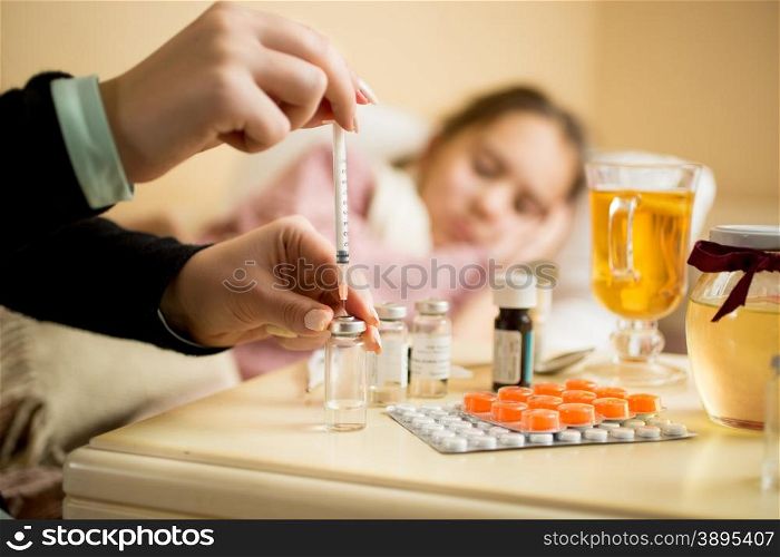 Macro shot of woman filling syringe from ampule with medicines next to patient&rsquo;s bed