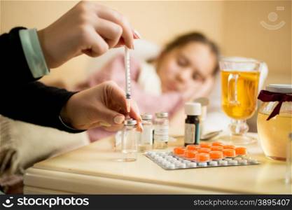 Macro shot of woman filling syringe from ampule with medicines next to patient&rsquo;s bed