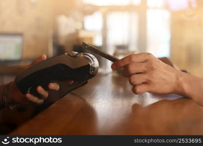 Macro unknown hand giving terminal to visitor for mobile phone payment indoor. Client hand paying bill with smartphone in blurred background. Cropped shot hands making contactless transaction inside. Macro unknown hand giving terminal to visitor for mobile phone payment indoor. Client hand paying bill with smartphone in blurred background. Cropped shot hands making contactless transaction inside.