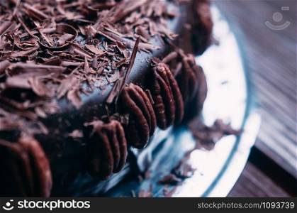 Macro view of delicious dark chocolate cake with beautiful icing, chips and pecan nuts on the side on the brown wooden table. Selective focus. Luxurious glaze. Image for menu or confectionery catalog
