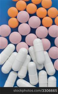 Macro view of white pink and orange pills on blue background.