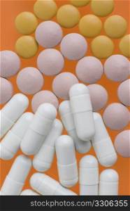 Macro view of white pink and orange pills on orange background.