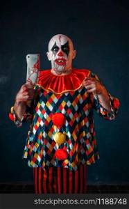 Mad bloody clown with meat cleaver and baseball bat, circus horror. Man with makeup in carnival costume, crazy maniac. Bloody clown with meat cleaver and baseball bat