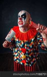 Mad bloody clown with meat cleaver and baseball bat, circus horror. Man with makeup in carnival costume, mad maniac. Bloody clown with meat cleaver and baseball bat