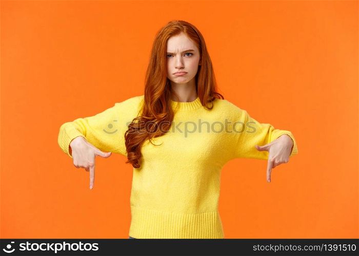 Mad unsatisfied cute redhead girlfriend, ginger girl in yellow sweater, frowning disappointed and angry, pointing down sulking, feeling offended with disapproval, standing orange background.. Mad unsatisfied cute redhead girlfriend, ginger girl in yellow sweater, frowning disappointed and angry, pointing down sulking, feeling offended with disapproval, standing orange background