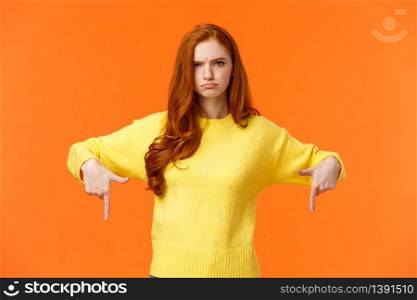 Mad unsatisfied cute redhead girlfriend, ginger girl in yellow sweater, frowning disappointed and angry, pointing down sulking, feeling offended with disapproval, standing orange background.. Mad unsatisfied cute redhead girlfriend, ginger girl in yellow sweater, frowning disappointed and angry, pointing down sulking, feeling offended with disapproval, standing orange background
