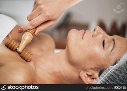 Maderotherapy anti-aging treatment of upper part of a woman&rsquo;s neck and torso with wooden roller . Maderotherapy Anti-Aging Treatment of Woman&rsquo;s Neck and Torso with Wooden Roller