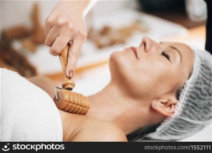 Maderotherapy anti-aging treatment of upper part of a woman&rsquo;s neck and torso with wooden roller . Maderotherapy Anti-Aging Treatment of Woman&rsquo;s Neck and Torso with Wooden Roller