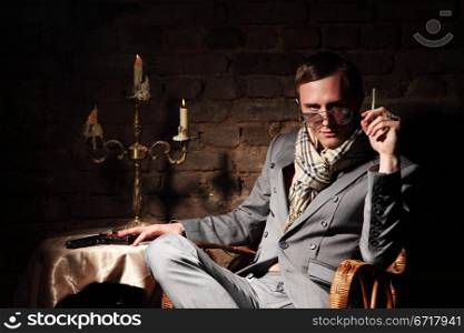 Mafioso. Man with a gun in a wicker chair on the background of an old brick wall