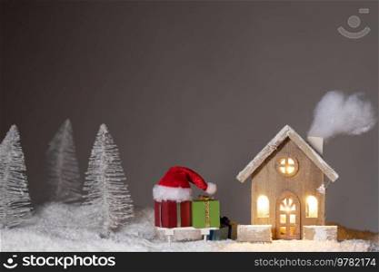 Magic Christmas card with toy wooden house in winter forest and gifts. Christmas toy house and gifts