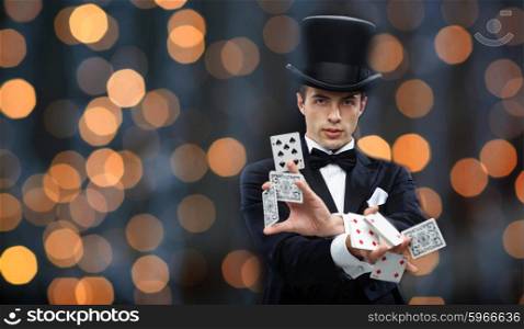 magic, gambling, casino, people and show concept - magician in top hat showing trick with playing cards over nigh lights background