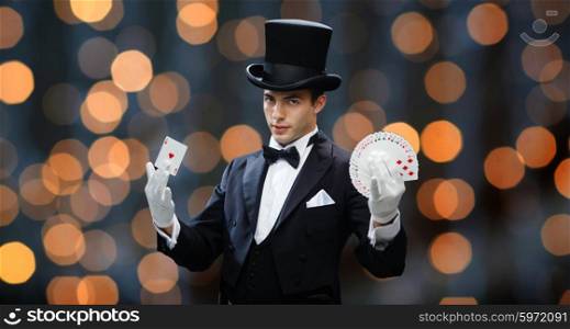 magic, performance, gambling, casino, people and show concept - magician in top hat showing trick with playing cards over nigh lights background