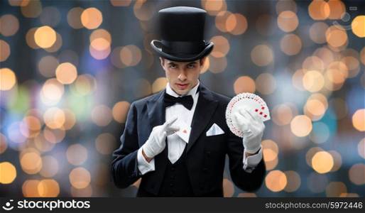 magic, performance, gambling, casino, people and show concept - magician in top hat showing trick with playing cards over nigh lights background