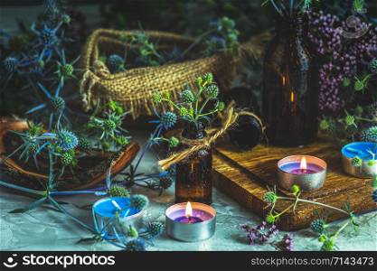 Magic potion in small bottle, blue eryngo and candles on dark background. Old pharmacy, esoteric or alchemic concept. Black magic and occult objects, alternative medicine or homeopathic