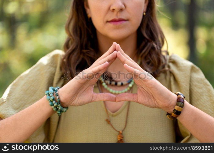 magic, spirituality and supernatural concept - close up of woman or witch making triangle of power gesture in forest. woman or witch performing magic ritual in forest