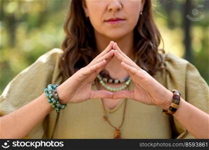 magic, spirituality and supernatural concept - close up of woman or witch making triangle of power gesture in forest. woman or witch performing magic ritual in forest