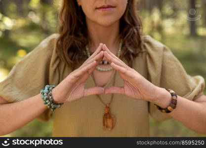 magic, spirituality and supernatural concept - close up of woman or witch making triangle of power gesture in forest. woman or witch performing magic ritual in forest