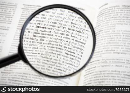 Magnifying glass focussed on the word &rsquo;insurance&rsquo; on the page of a generic dictionary.