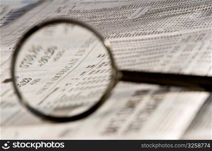 Magnifying glass highlighting investment stock quotes in business section of newspaper.