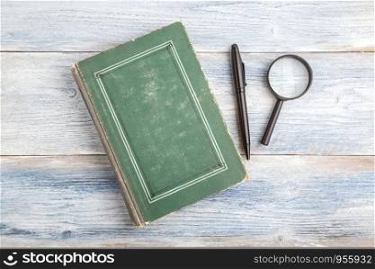 magnifying glass, pen and book on light blue old wooden background. top view. flat lay