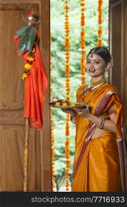 Maharashtrian woman in traditional dress celebrating gudi padwa festival holding a pooja plate looking at camera.