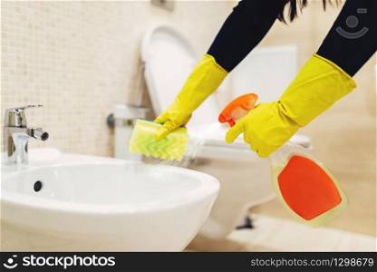 Maid hands in rubber gloves cleans the bidet with a cleaning spray, hotel restroom interior on background. Professional housekeeping service, charwoman, sanitary processing. Maid cleans the bidet with a cleaning spray
