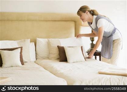 Maid making bed in hotel room smiling