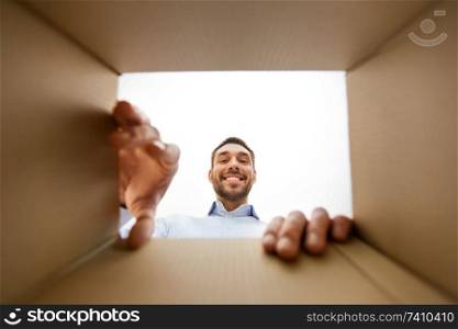 mail delivery and surprise concept - smiling man taking something out of parcel box, from below. smiling man taking something out of parcel box
