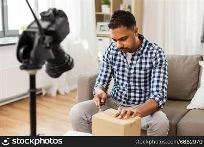 mail delivery, shipment and blogging concept - indian male blogger opening parcel box and recording video by camera at home. male video blogger opening parcel box at home