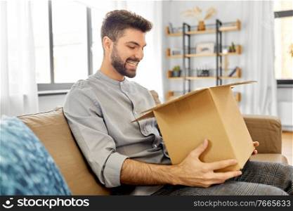 mail delivery, shipment and people concept - happy smiling man opening parcel box at home. happy smiling man opening parcel box at home