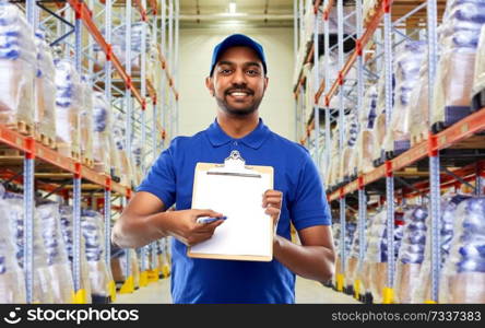 mail service and shipment concept - happy indian delivery man or warehouse worker with clipboard in blue uniform over goods background. delivery man or warehouse worker with clipboard