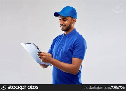 mail service and shipment concept - happy indian delivery man with clipboard in blue uniform over grey background. happy indian delivery man with clipboard in blue