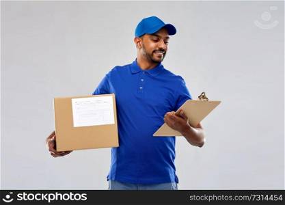 mail service and shipment concept - happy indian delivery man with parcel box and clipboard in blue uniform over grey background. indian delivery man with parcel box and clipboard