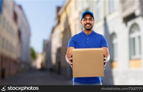 mail service and shipment concept - happy indian delivery man with parcel box in blue uniform over old tallinn city street background. happy indian delivery man with parcel box in city