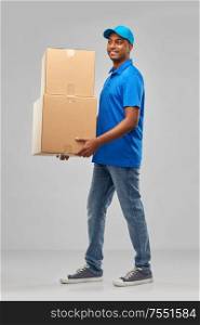 mail service and shipment concept - happy indian delivery man with parcel boxes in blue uniform over grey background. happy indian delivery man with parcel boxes