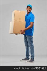 mail service and shipment concept - happy indian delivery man with parcel boxes in blue uniform over grey background. happy indian delivery man with parcel boxes