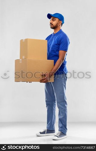 mail service and shipment concept - indian delivery man with parcel boxes in blue uniform over grey background. indian delivery man with parcel boxes in blue