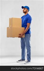 mail service and shipment concept - indian delivery man with parcel boxes in blue uniform over grey background. indian delivery man with parcel boxes in blue