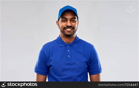 mail service, job and people concept - happy indian delivery man in blue uniform over grey background. happy indian delivery man in blue uniform