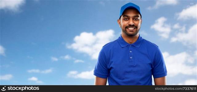 mail service, job and people concept - happy indian delivery man in blue uniform over sky and clouds background. happy indian delivery man in blue uniform over sky