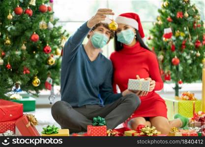 Main focus of gold Christmas ball decorating of Christmas tree that hold by man with hygiene mask and sit near his couple woman during celebration of the festival with new normal lifestyle from covid.