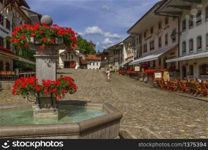 Main street and fountain in Gruyere village in Fribourg canton by beautiful day, Switzerland. Gruyere village in Fribourg canton, Switzerland