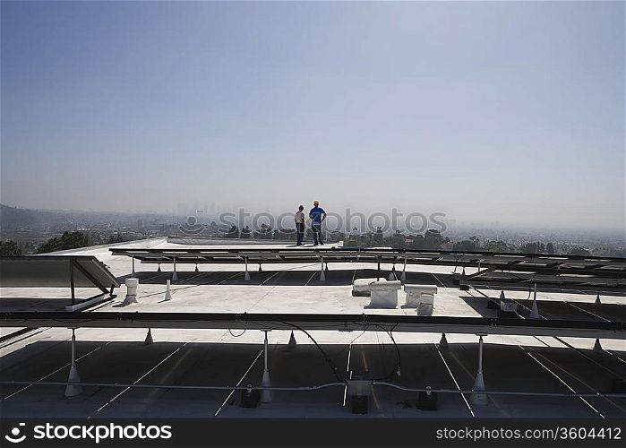 Maintenance workers stand with solar array on rooftop in Los Angeles California