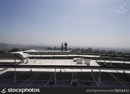 Maintenance workers stand with solar array on rooftop in Los Angeles California