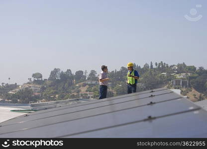 Maintenance workers stand with solar array on rooftop in Los Angeles California